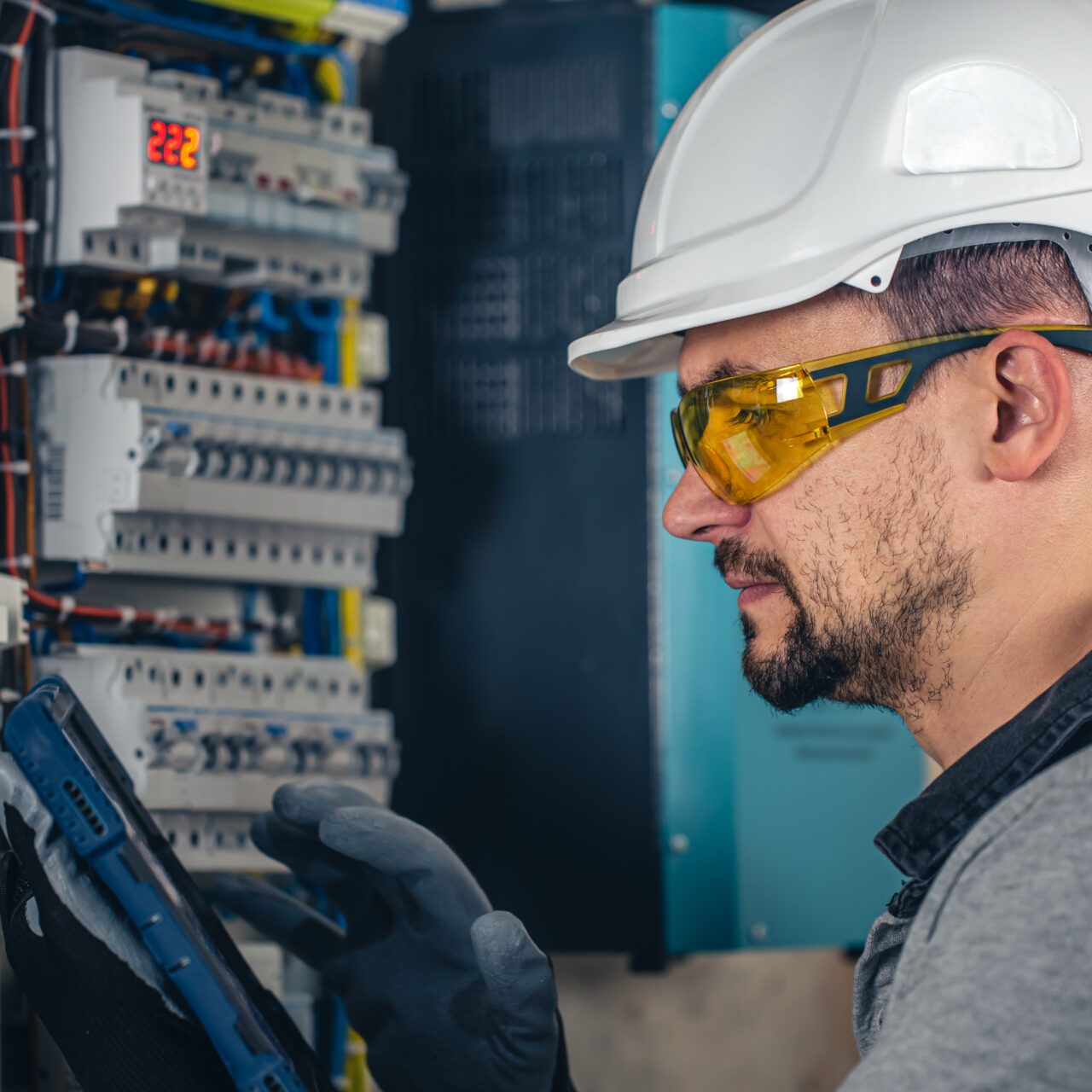Man, an electrical technician working in a switchboard with fuses. Installation and connection of electrical equipment. Professional uses a tablet.